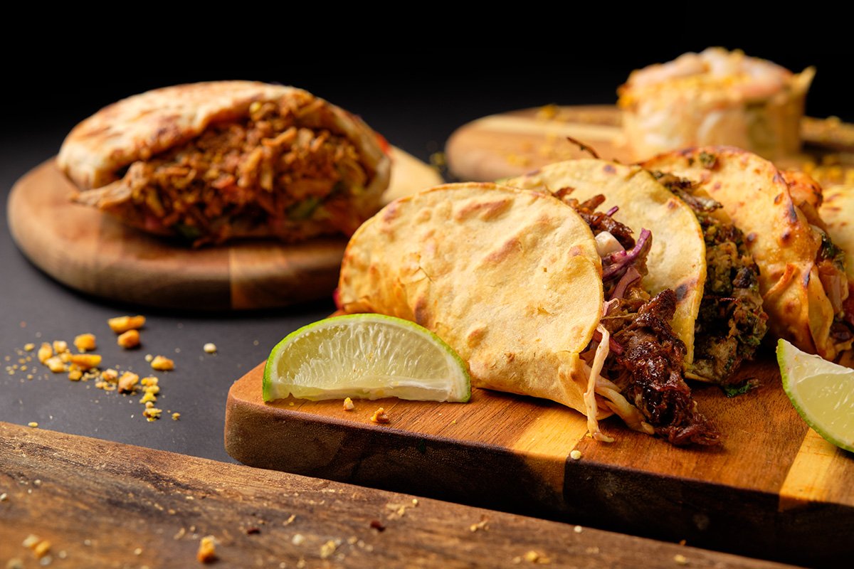 Taco de carne sobre tabla de madera junto platos cubanos